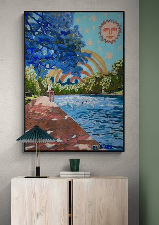 Colorful painting with a rainbow, sun, and riverside scene displayed above a light wooden cabinet.