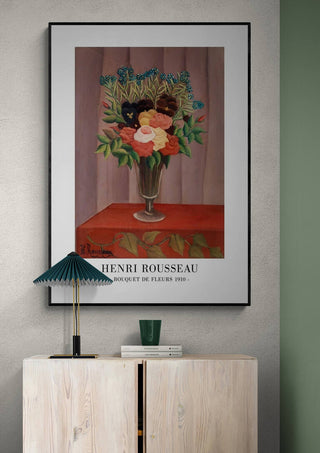 Framed print of Henri Rousseau's "Bouquet De Fleurs 1910" displayed above a light wooden cabinet.
