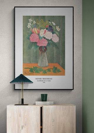 Framed print of "Flowers In a Vase" by Henri Rousseau hanging above a light wooden cabinet.