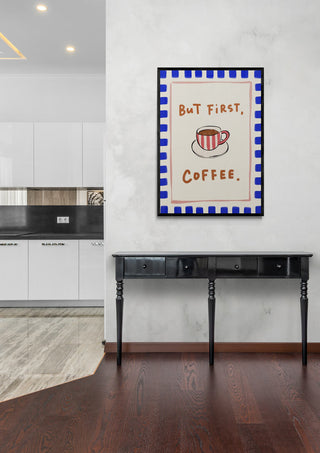 Framed "But First, Coffee" print with a coffee cup illustration hanging above a black console table in a modern room.