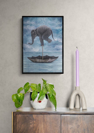 Elephant in Balance art print by Coco de Paris, framed and displayed above a cabinet with decor and a plant.